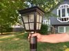 Hand holding a Kemeco Solar Post Light outside in front of a house