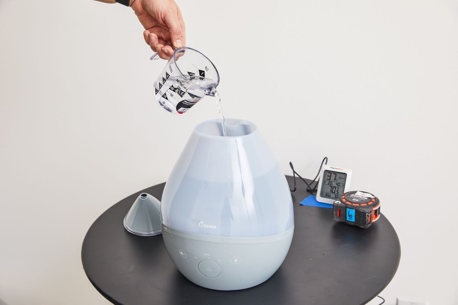 Hand pouring water into a Crane 4-in-1 Drop Ultrasonic Cool Mist Humidifier EE-8086 on a table 