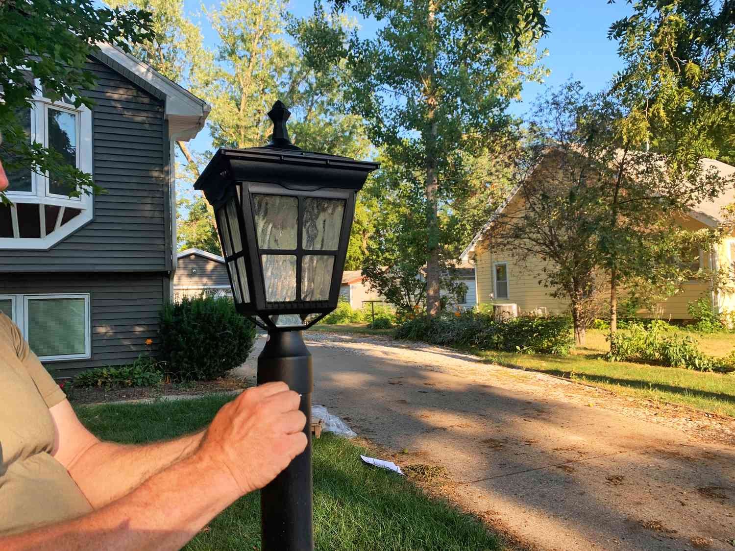 Hands screwing in the Kemeco Solar Post Light displayed in front of a house