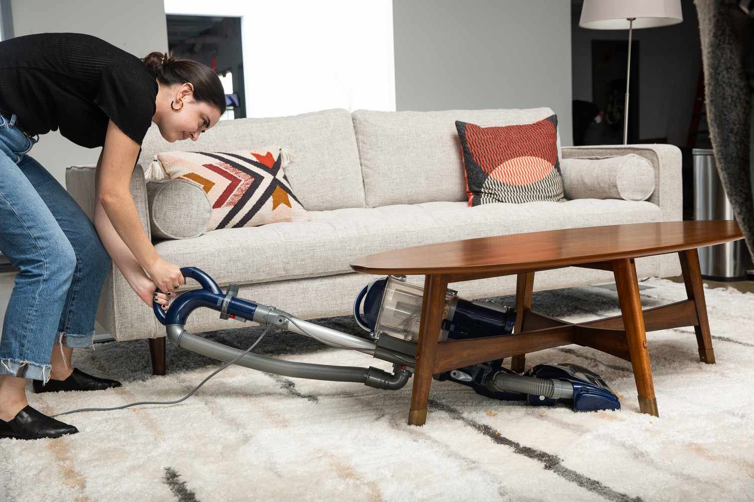 Person using Shark NV360 Navigator Lift-Away Deluxe Upright Vacuum to clean a striped carpet under a wooden table