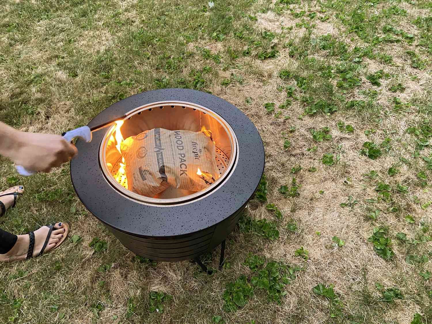 Hand lighting a fire inside the Tiki Low-Smoke Portable Fire Pit outside 