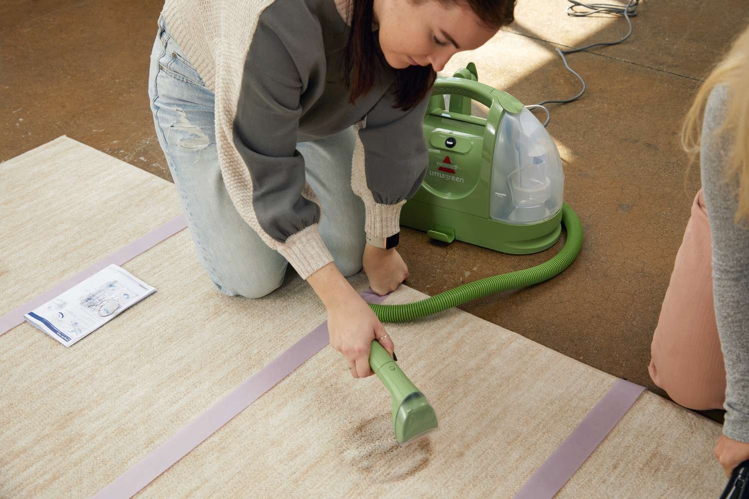 Person cleaning a brown carpet stain with the Bissell Little Green Cleaner