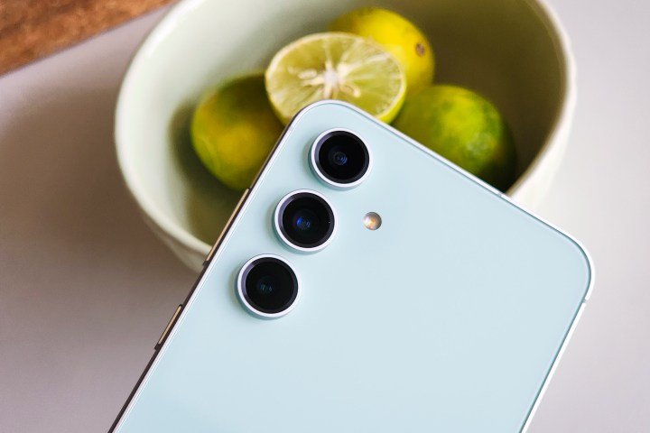 Rear camera setup on the Samsung Galaxy S23 FE Mint Green held in front of a bowl of lemons.