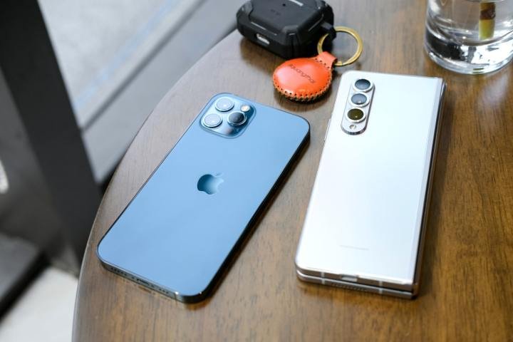 A Samsung Galaxy phone and an iPhone side-by-side on a desk, next to an Apple AirTag.