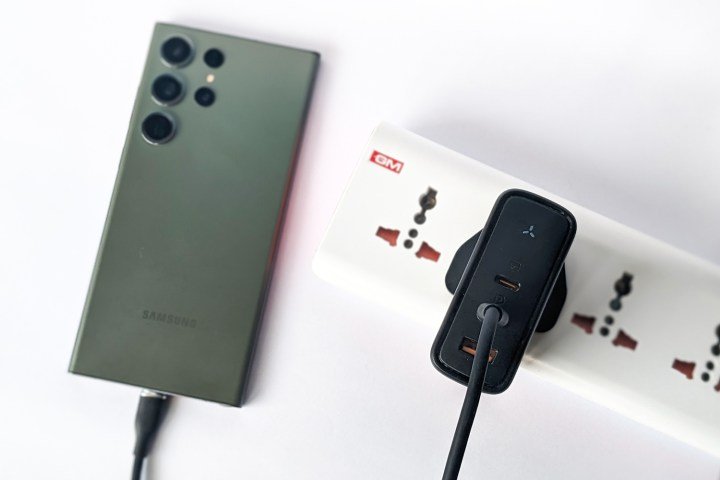 Voltme Revo 140 GaN charger plugged into a power strip and kept alongside a green Samsung Galaxy S23 Ultra on a white background.