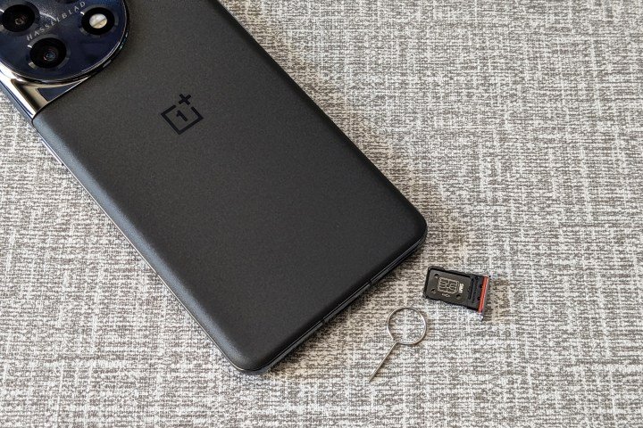OnePlus 11 titan black color with the SIM tray ejected and kept on a white and gray table top.