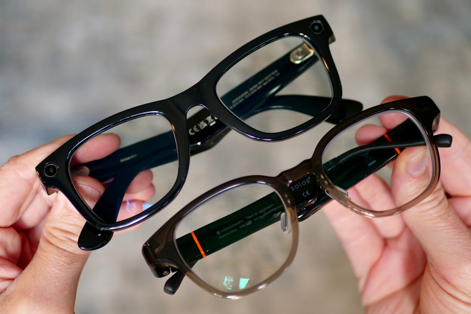 A person holding the Ray-Ban Meta and Solos AirGo 3 smart glasses.