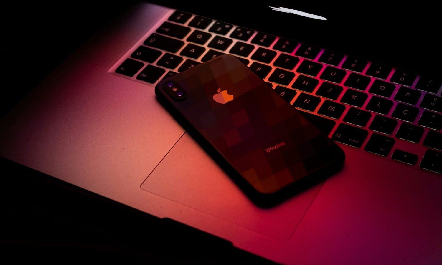 A MacBook and iPhone in dark red light.