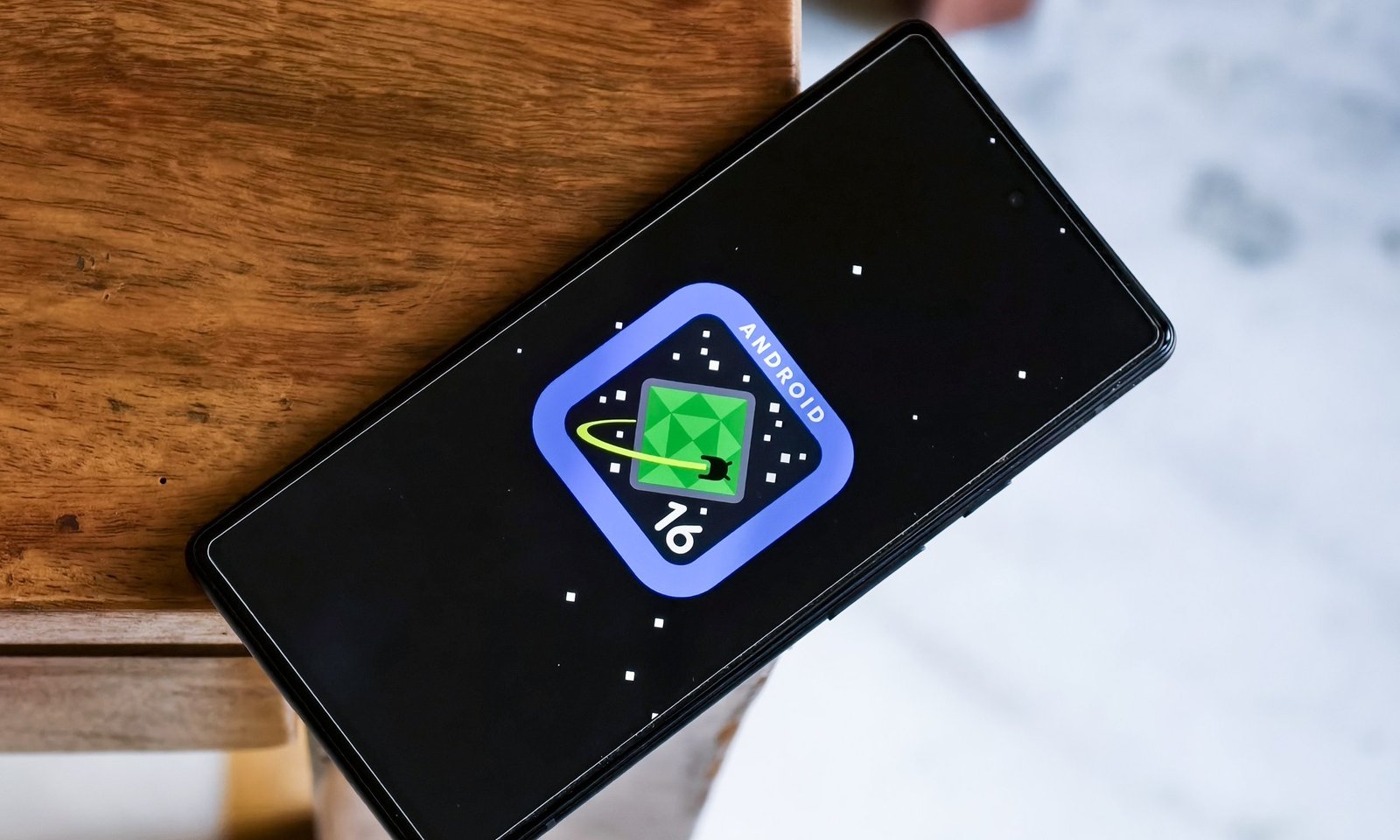 Android 16 logo on Google Pixel 6a kept on the edge of a table.
