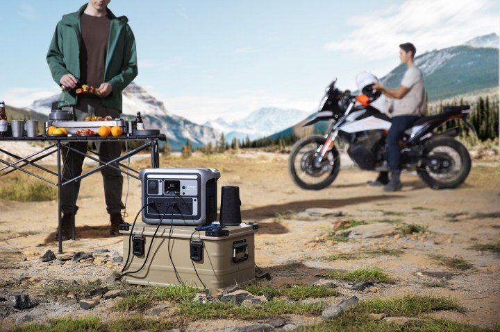Anker solix power bank setup for camping while a man cooks and another sits atop a motorcycle