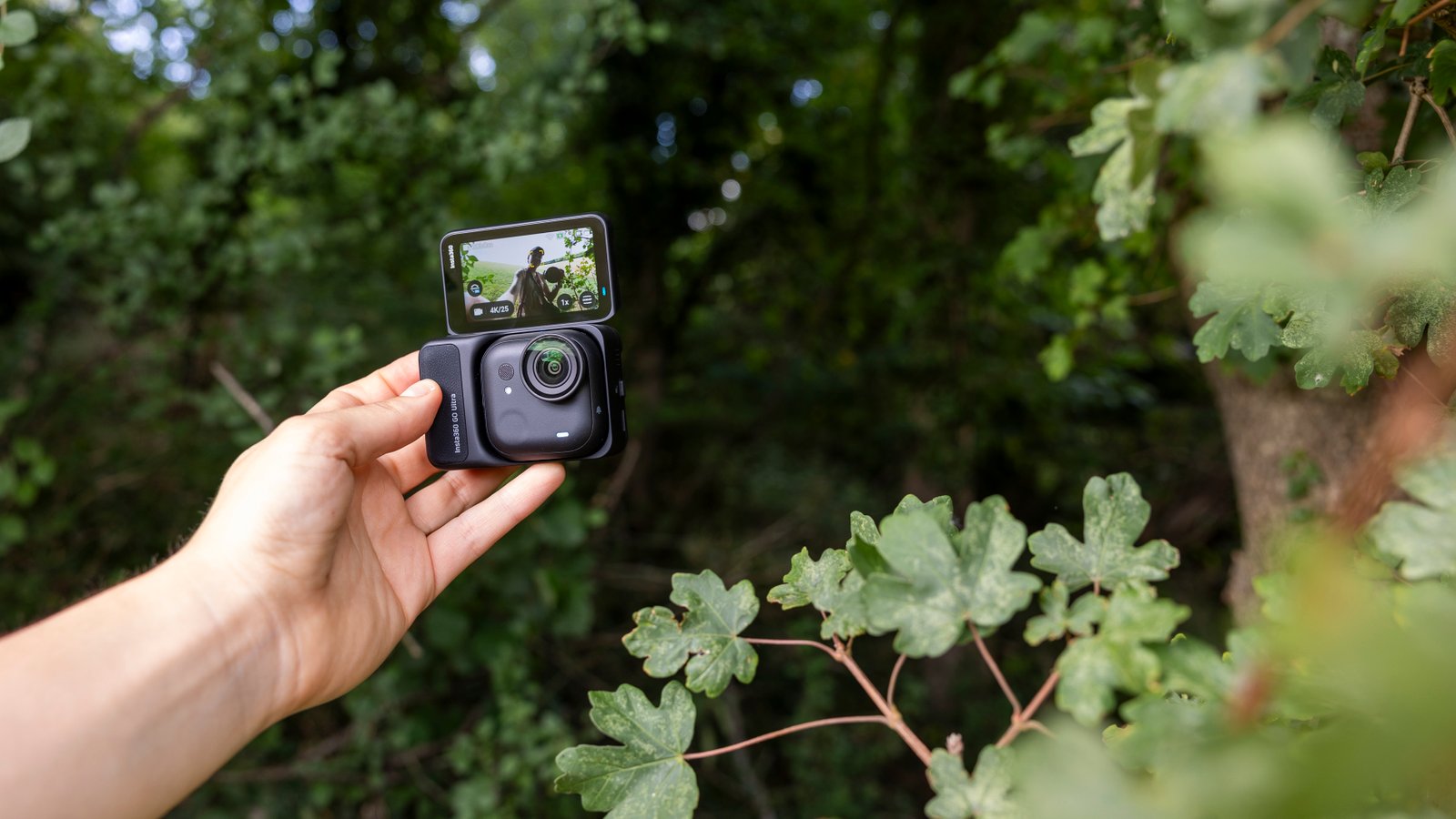 The Insta360 GO Ultra camera held by a female photographer against a green wooded backdrop